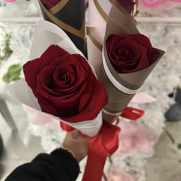 Three red roses wrapped in decorative paper with a red ribbon