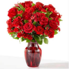 Red roses and carnations arranged in a red glass vase