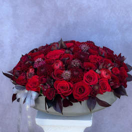 Large red rose arrangement in a shallow white container with a ribbon