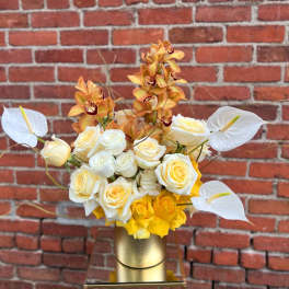 White and yellow roses with orange orchids in a gold vase