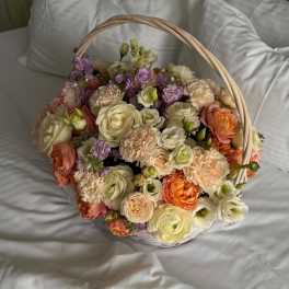 Basket of pastel roses, carnations, and purple blooms on white bedding