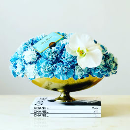 Blue and white floral arrangement in a gold bowl on stacked books