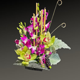 Tall orchid arrangement with lime green and magenta blooms in a black container