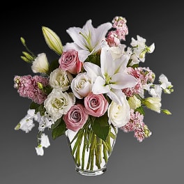 Pink and white roses with lilies in a clear glass vase