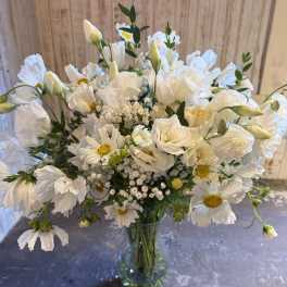 Tall glass vase of white daisylike blooms and lisianthus with yellow centers in a loose, airy arrangement