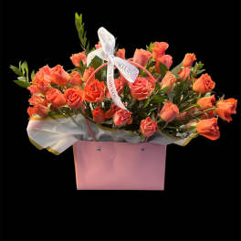Coral roses arranged in a pink gift box with a ribbon bow