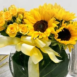 Yellow sunflowers and roses in a round glass vase with a yellow ribbon