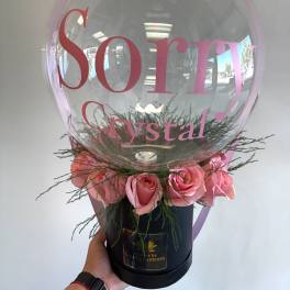 Pink roses arranged around a clear balloon with a pink bow