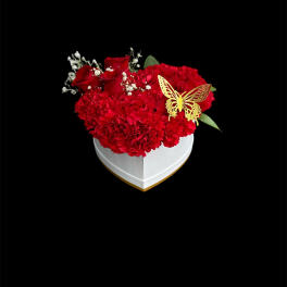 Red carnations and roses in a white heart-shaped box with a butterfly accent