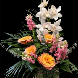 Orange roses and pink orchids in a tall vase arrangement