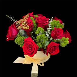 Red roses arranged in a round box with a gold ribbon and butterfly accent