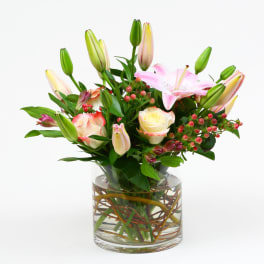 Pink lilies and cream roses with red berries arranged in a clear glass cylinder vase