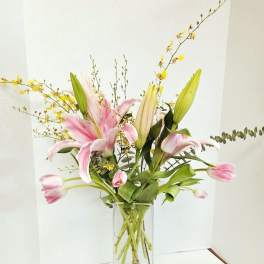 Pink lilies in a tall glass vase with yellow branching accents