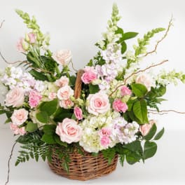 Pastel pink and white flower basket with roses, snapdragons, and other blooms in a woven wicker basket