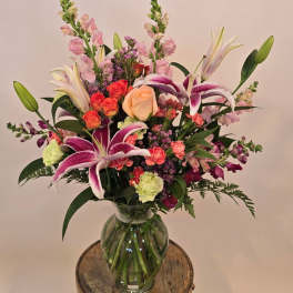 Tall mixed bouquet with pink lilies, roses, carnations, and snapdragons in a clear glass vase