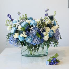 Blue and white floral arrangement in a glass vase with starfish accents