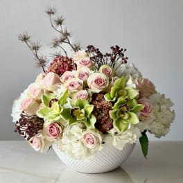 Bouquet of pink roses, white hydrangeas, and green orchids in a white vase