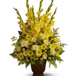 Tall yellow and white floral arrangement with gladiolus, roses, and daisies in a brown urn