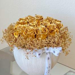 Gold roses in a white textured vase with a white ribbon