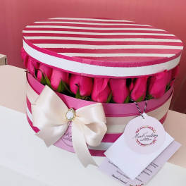 Pink roses arranged in a striped round gift box with a white bow