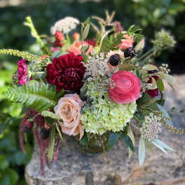 Bouquet of red, pink, and peach flowers with berries in a vase