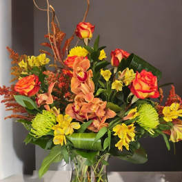 Mixed bouquet of orange roses, yellow flowers, and orchids in a glass vase