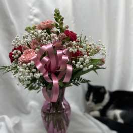 Pink and red mixed bouquet in a purple glass vase with a pink ribbon