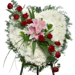 Heart-shaped white chrysanthemum standing spray with red roses and pink lilies on a metal easel.