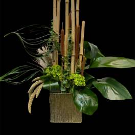 Tall tropical arrangement with bamboo stalks and broad green leaves in a gold vase