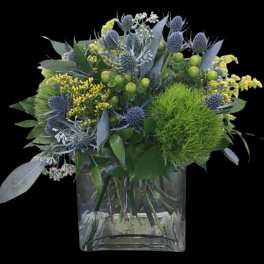 Blue thistle and yellow filler flowers in a clear square vase