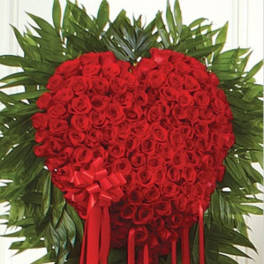 Heart-shaped red rose arrangement with a red ribbon bow and trailing ribbons