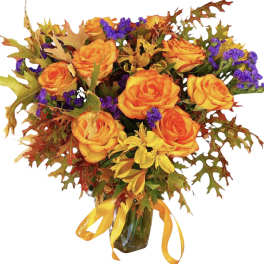 Orange roses in a glass vase with autumn leaves and purple filler flowers