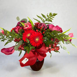 Red and pink mixed bouquet in a dark vase with a red ribbon