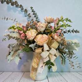 Blush roses and daisies in a white vase with a gold ribbon bow