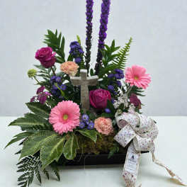 Floral arrangement with pink gerbera daisies, roses, and a cross centerpiece