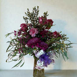 Purple and pink flower arrangement in a glass vase with a ribbon