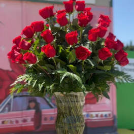 Tall vase arrangement of red roses with fern foliage