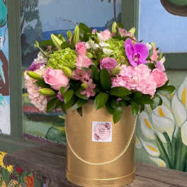 Pink and green floral arrangement in a gold hatbox