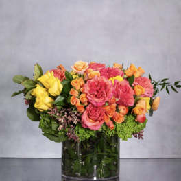 Mixed bouquet of pink, yellow, and orange roses in a glass vase