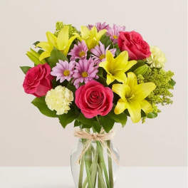 Bouquet of pink roses, yellow lilies, and purple daisies in a glass vase