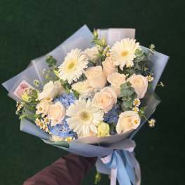 Bouquet of cream roses, white daisies, and blue hydrangeas wrapped in pale blue paper