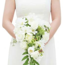 Bride in a white dress holding a cascading white rose bouquet with green accents