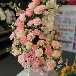 Pink and white rose arrangement with orchids in a white vase