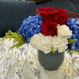Red roses, blue hydrangeas, and white carnations in a dark vase