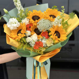 Bouquet of sunflowers, roses, and white blooms wrapped in yellow and green paper