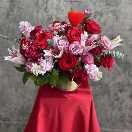 Red and pink rose bouquet with lilies and a heart topper in a basket