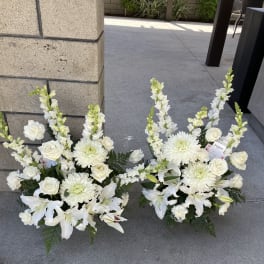 Two white floral arrangements with lilies, roses, and chrysanthemums on the ground.