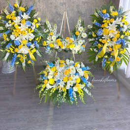 Three yellow, white, and blue floral funeral sprays with ribbons
