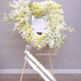 White floral wreath on a stand with lilies and roses