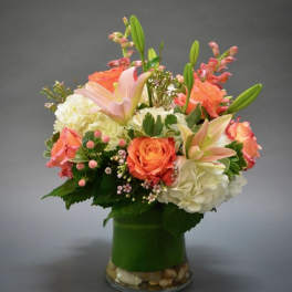 Bouquet of orange roses, lilies, and white hydrangeas in a glass vase